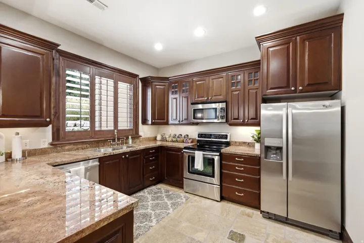 Rich wood cabinetry with crown molding, stainless steel appliances, polished stone countertops, undermount sink, and recessed lighting