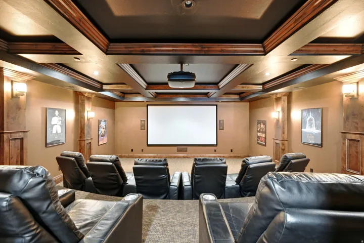 Recessed projector screen with integrated projector, coffered ceiling with wood-paneled beams, wall sconces, and built-in wood-paneled columns