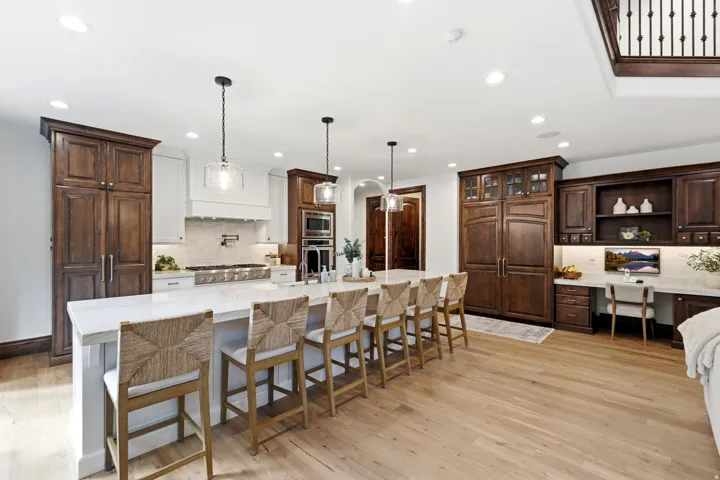 Light wood-finish flooring, a large kitchen island with seating, dark wood cabinetry, a built-in desk area, and recessed lighting