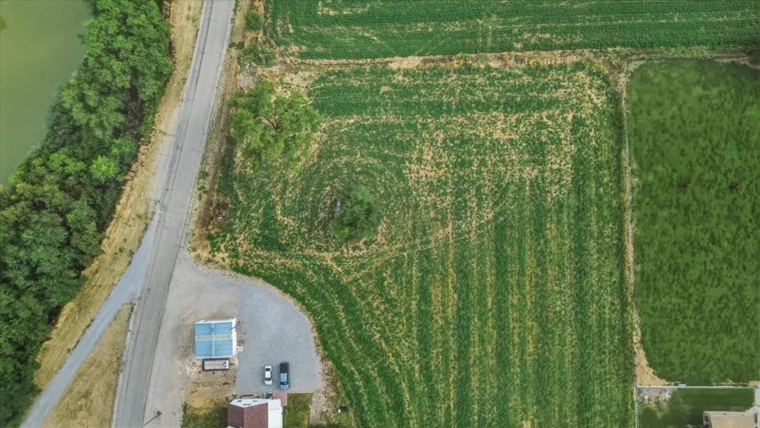 Expansive agricultural land featuring cultivated fields, a gravel driveway, and a partially visible structure with a light-colored roof