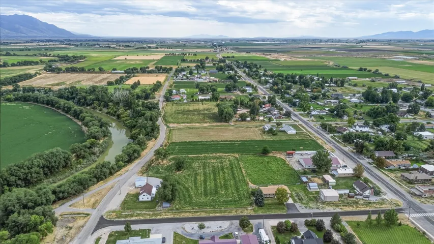 Expansive rural landscape featuring a river, surrounding green fields, established residential areas, and distant mountains