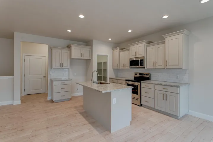 Kitchen featuring extensive light cabinetry, light wood-finish flooring, recessed lighting, a central island with a sink, and stainless steel appliances