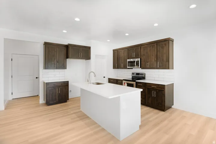 Kitchen featuring dark wood-finish cabinetry, white countertops, subway tile backsplash, and stainless steel appliances