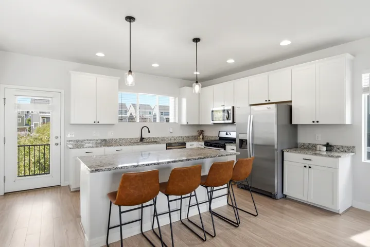 Kitchen featuring white cabinetry, stainless steel appliances, a center island with countertop seating, wood-finish flooring, and pendant lighting