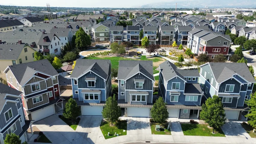 Community setting with a green space, mature trees, and residential buildings featuring varied siding materials and architectural styles