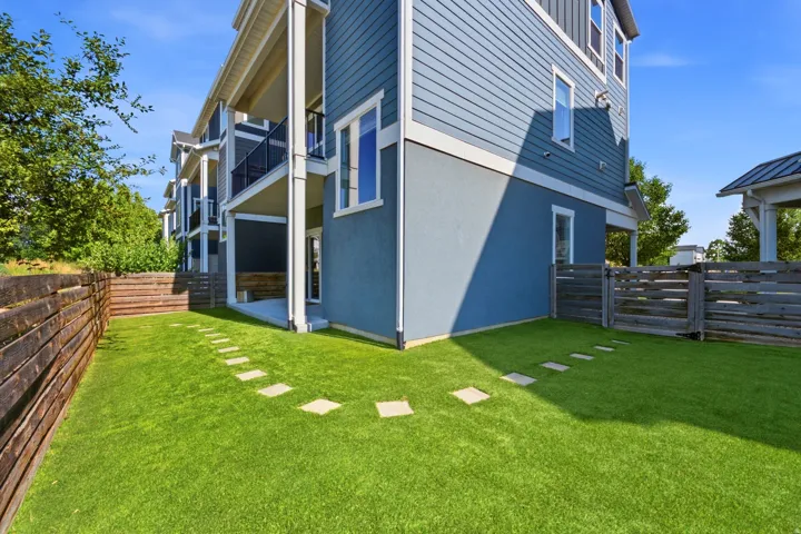 Expansive backyard featuring artificial turf, stepping stones, a wooden retaining wall, and horizontal slat fencing