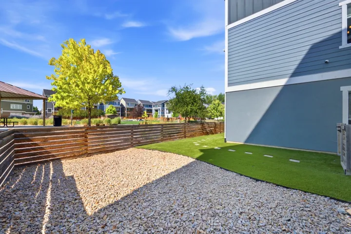 Blue siding exterior, wood horizontal slat fencing, gravel ground cover, artificial turf, and a covered outdoor structure