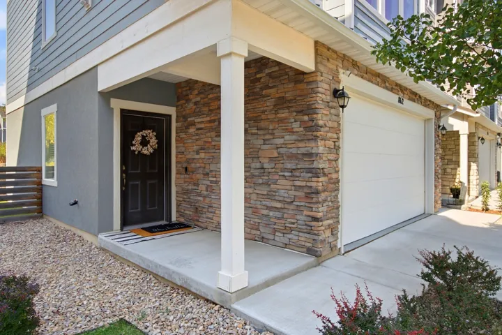 Stone veneer accent, stucco siding, horizontal siding, attached garage, and covered entry