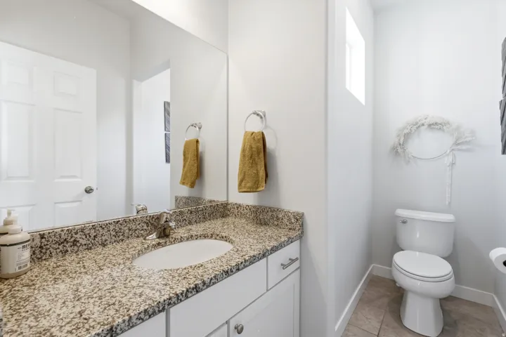 White vanity cabinetry with brushed nickel hardware, light-toned granite countertop with an undermount sink, and a large wall-mounted mirror