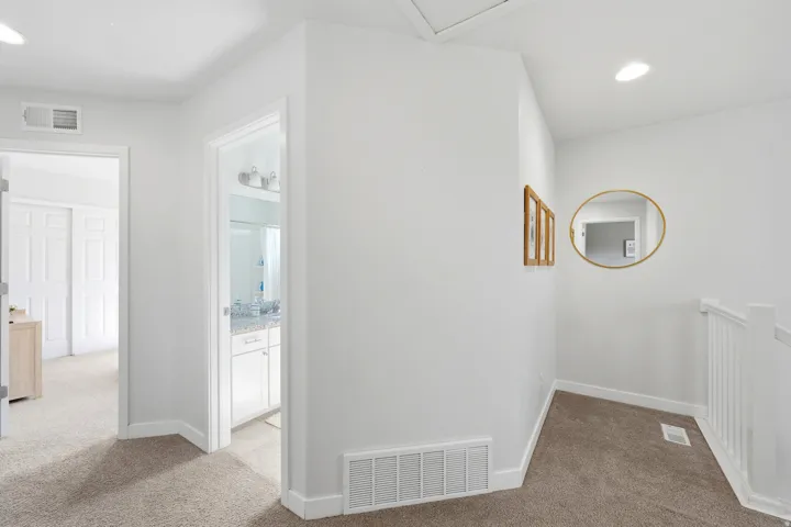 Carpeted hallway with white walls and trim, leading to a room with a white sliding closet door