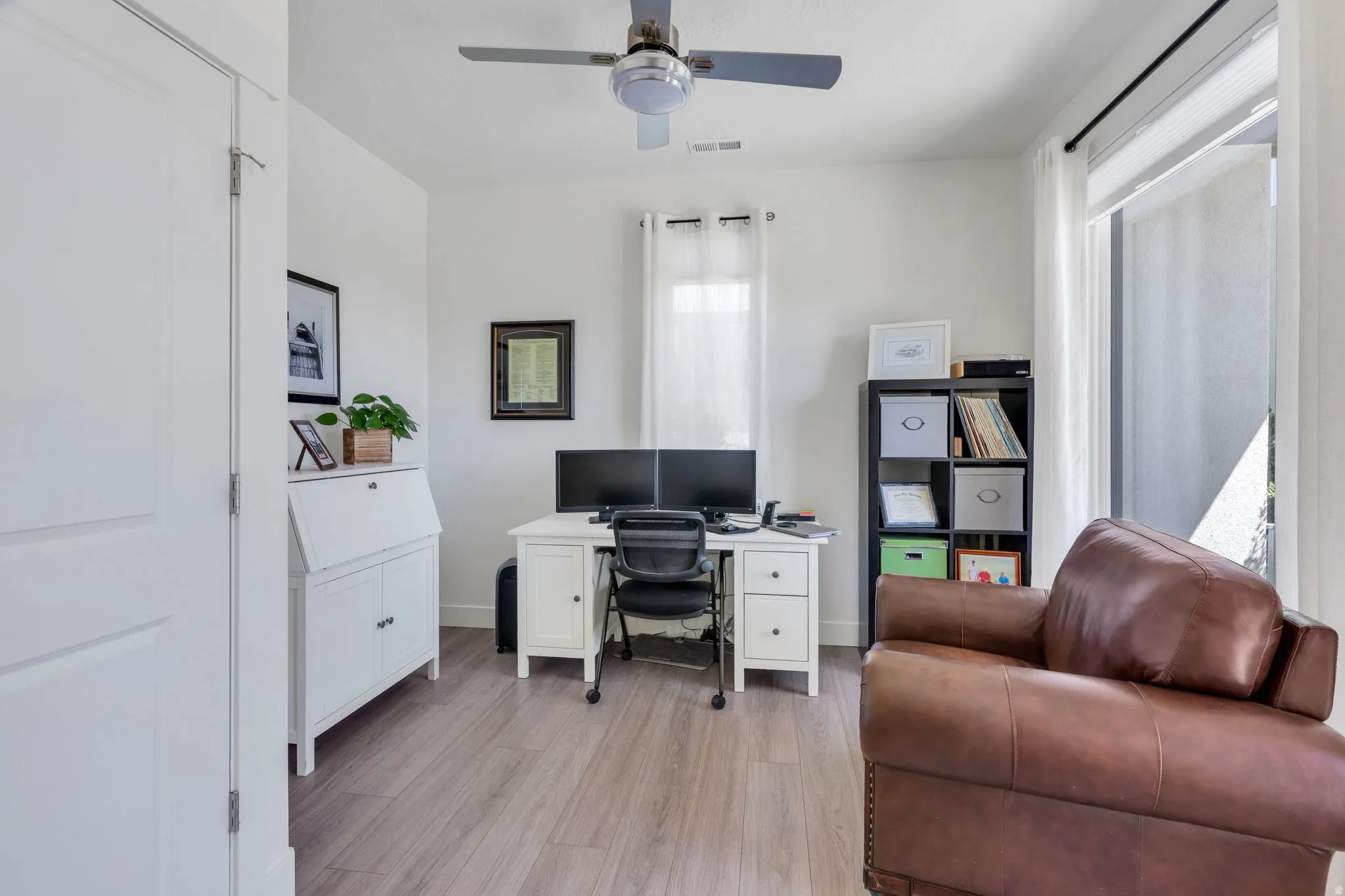 Light wood-finish flooring, white walls, and a ceiling fan with integrated lighting