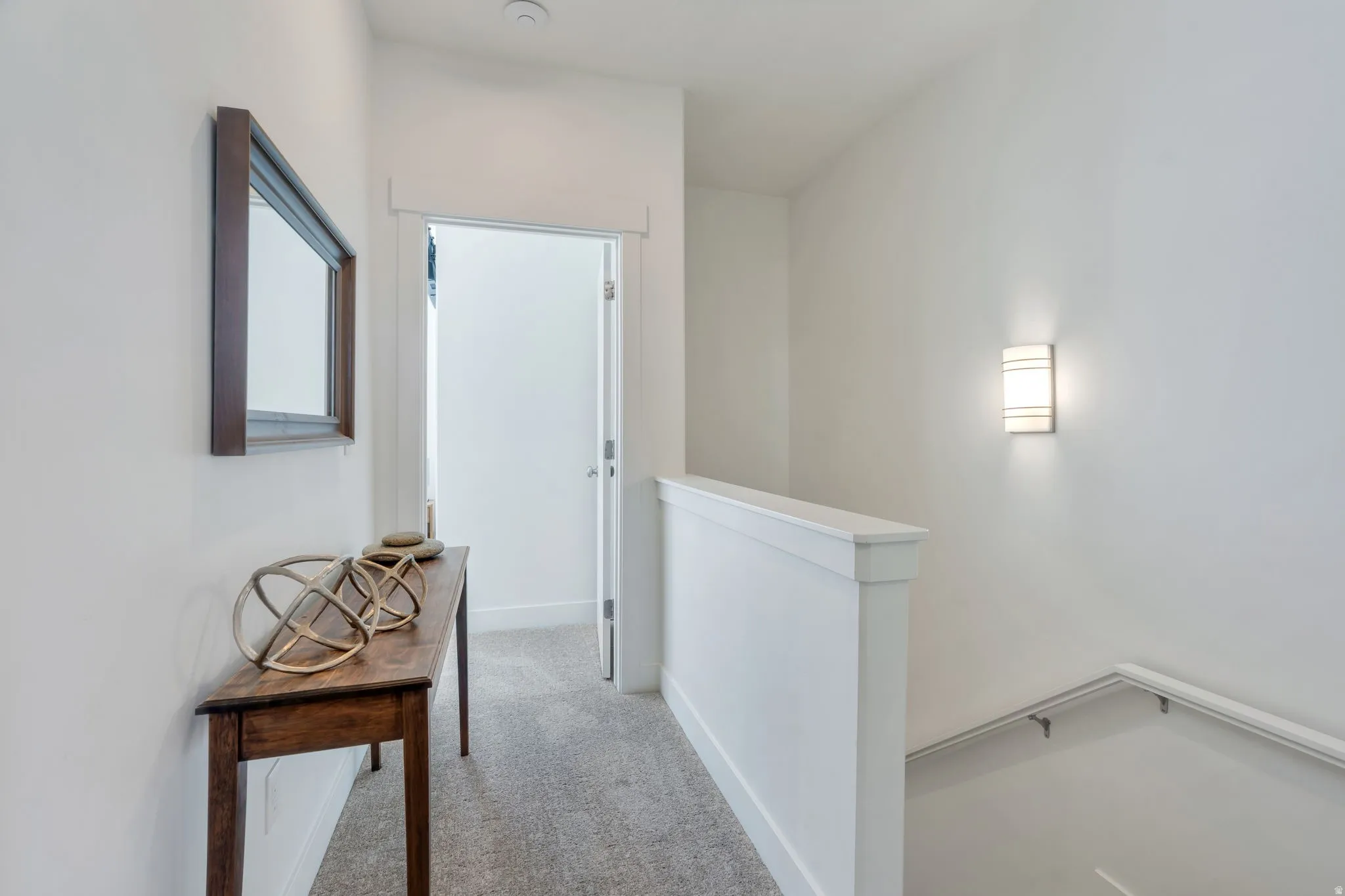 Carpeted hallway with white walls and trim, featuring a contemporary wall sconce and a white painted handrail