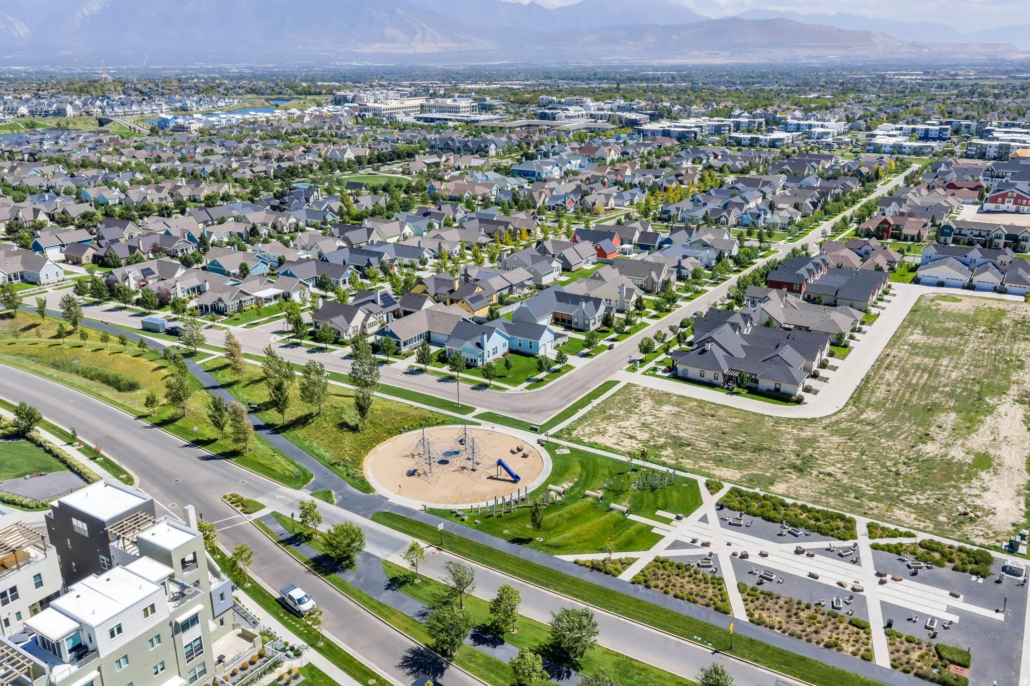 Expansive community featuring residential streets, a park with playground equipment, designated green spaces, and mountain backdrops