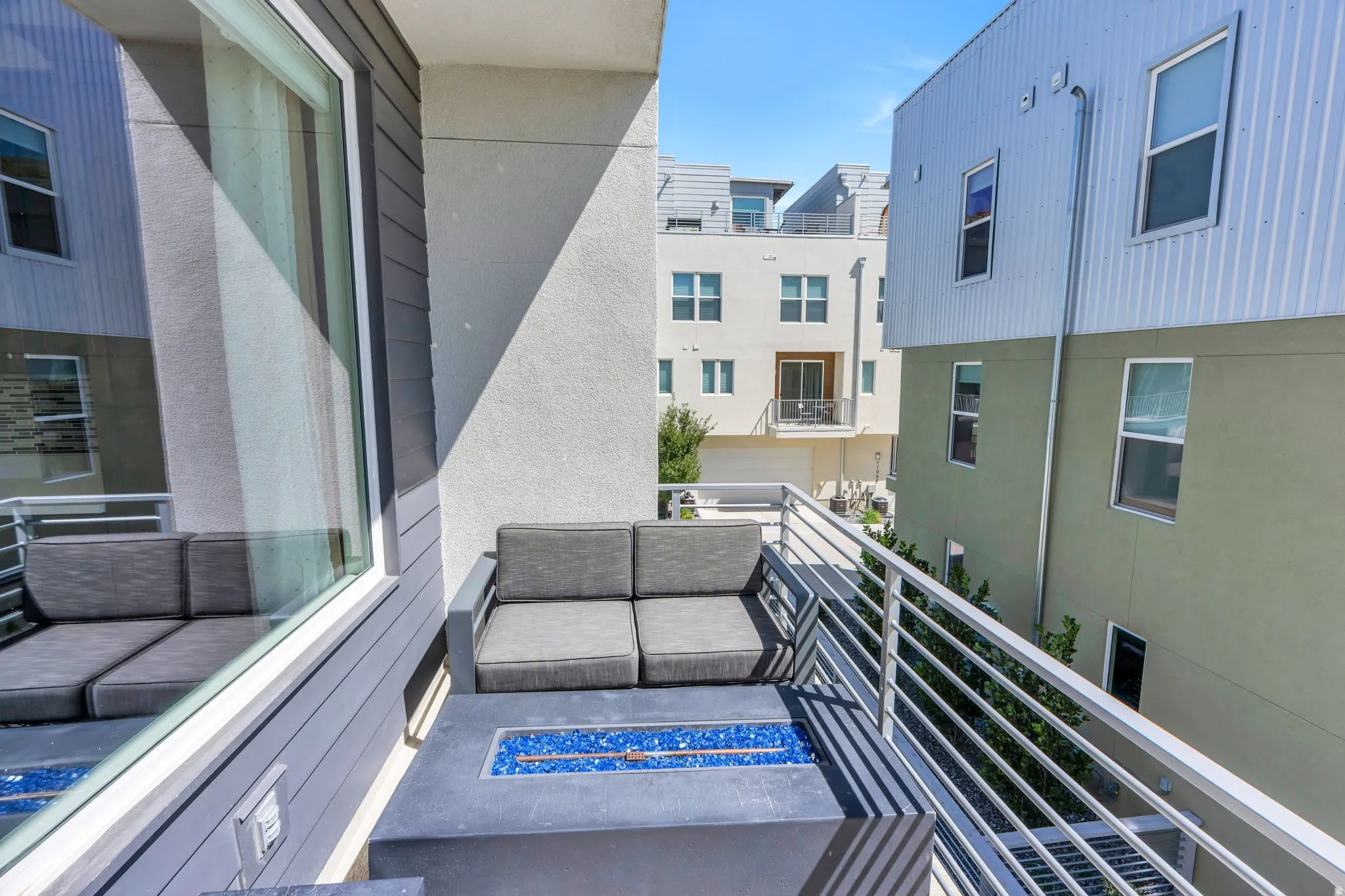 Balcony featuring a built-in fire pit with blue glass rocks, a modern metal railing, and a large window