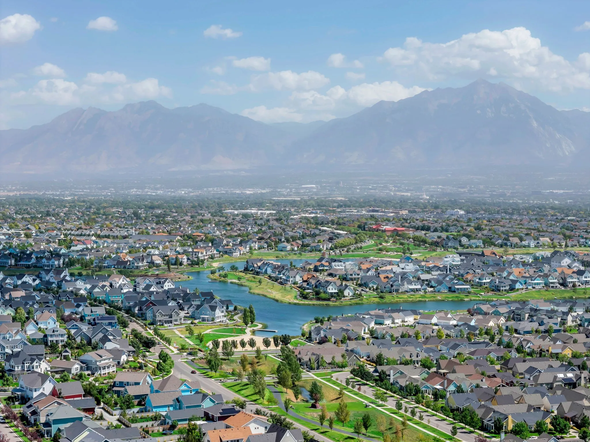 Expansive residential area with a prominent mountain backdrop, featuring a central body of water, extensive green spaces, and a network of paved roads