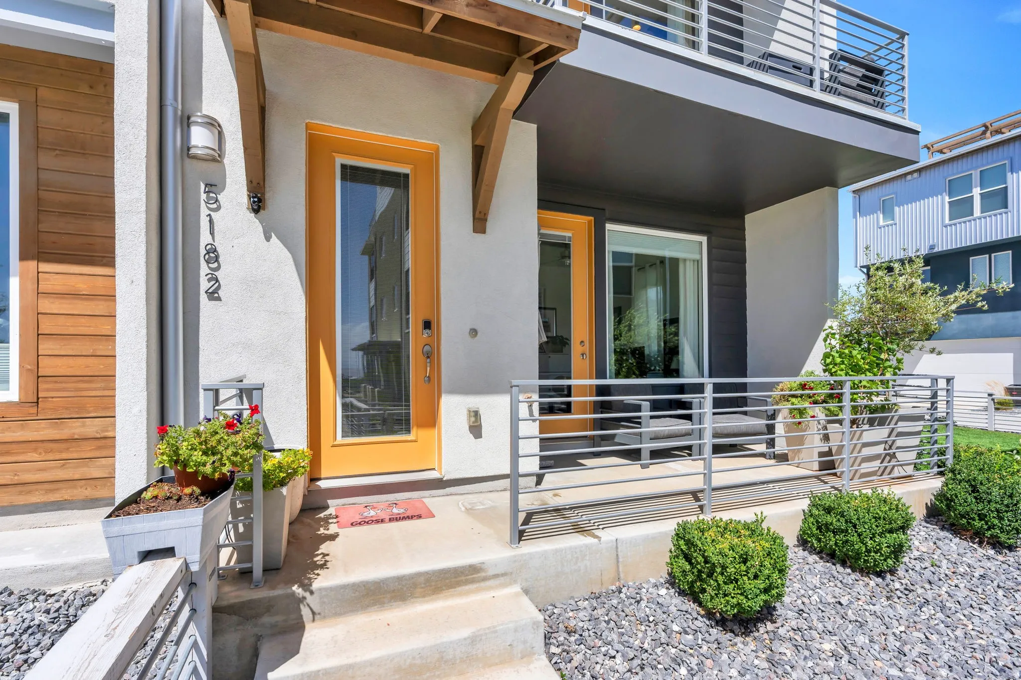 Modern exterior with wood-finish siding, a bright yellow entry door, and a private balcony featuring a metal railing