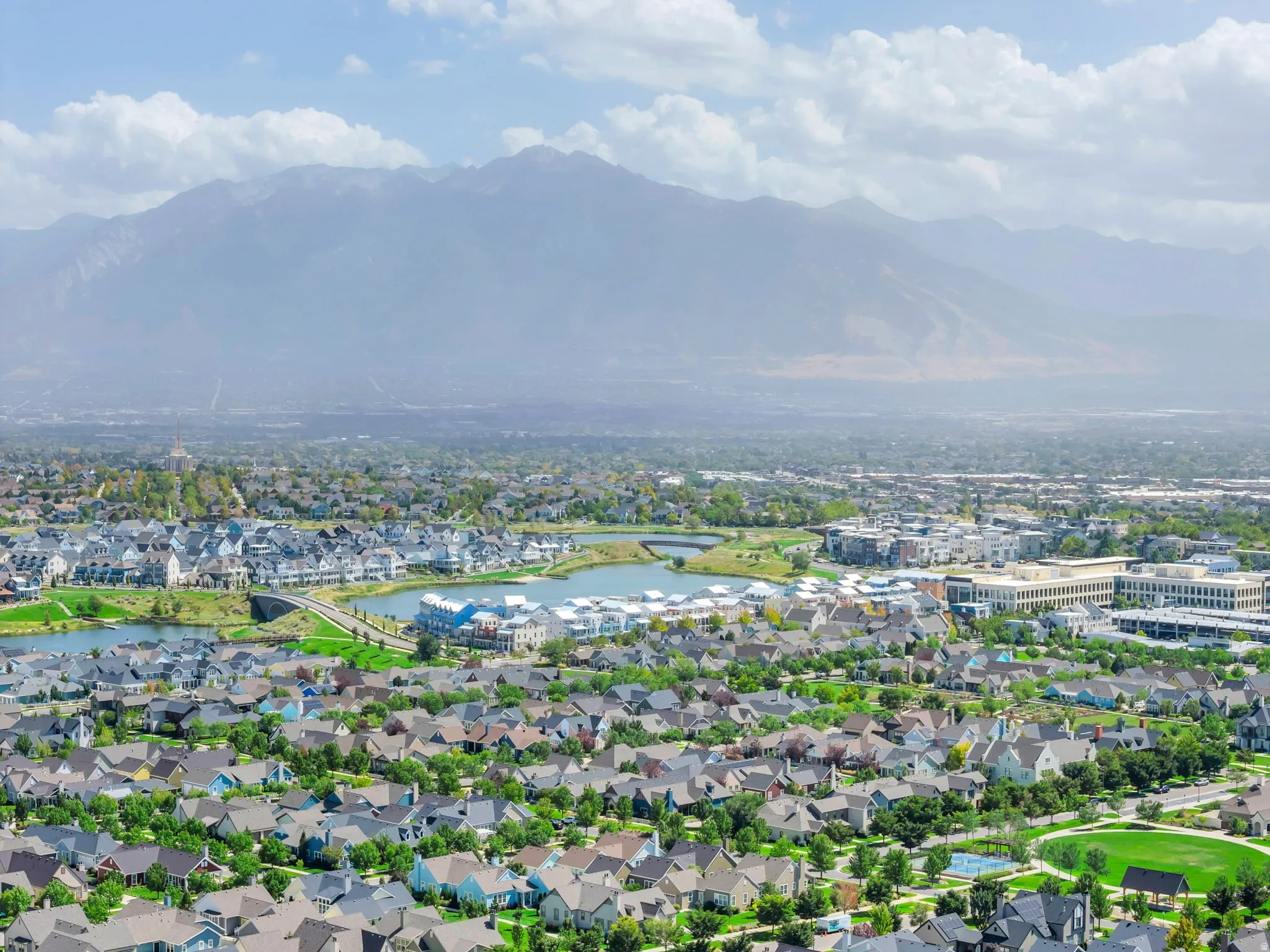 Expansive community featuring diverse residential architecture, a prominent lake, lush green spaces, and mountain scenery