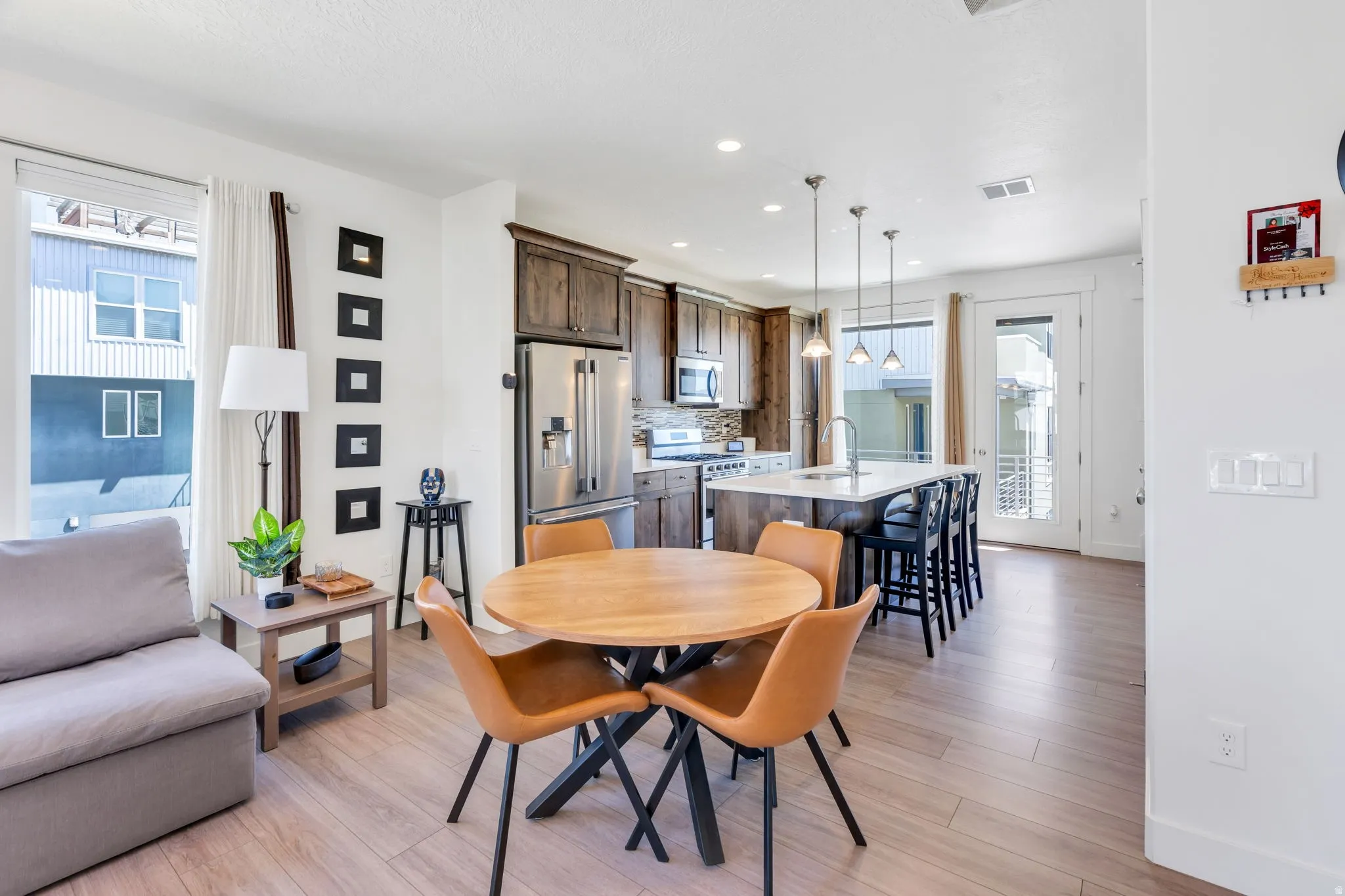Open-concept living space with wood-finish flooring, a kitchen island with pendant lighting, stainless steel appliances, and dark wood cabinetry