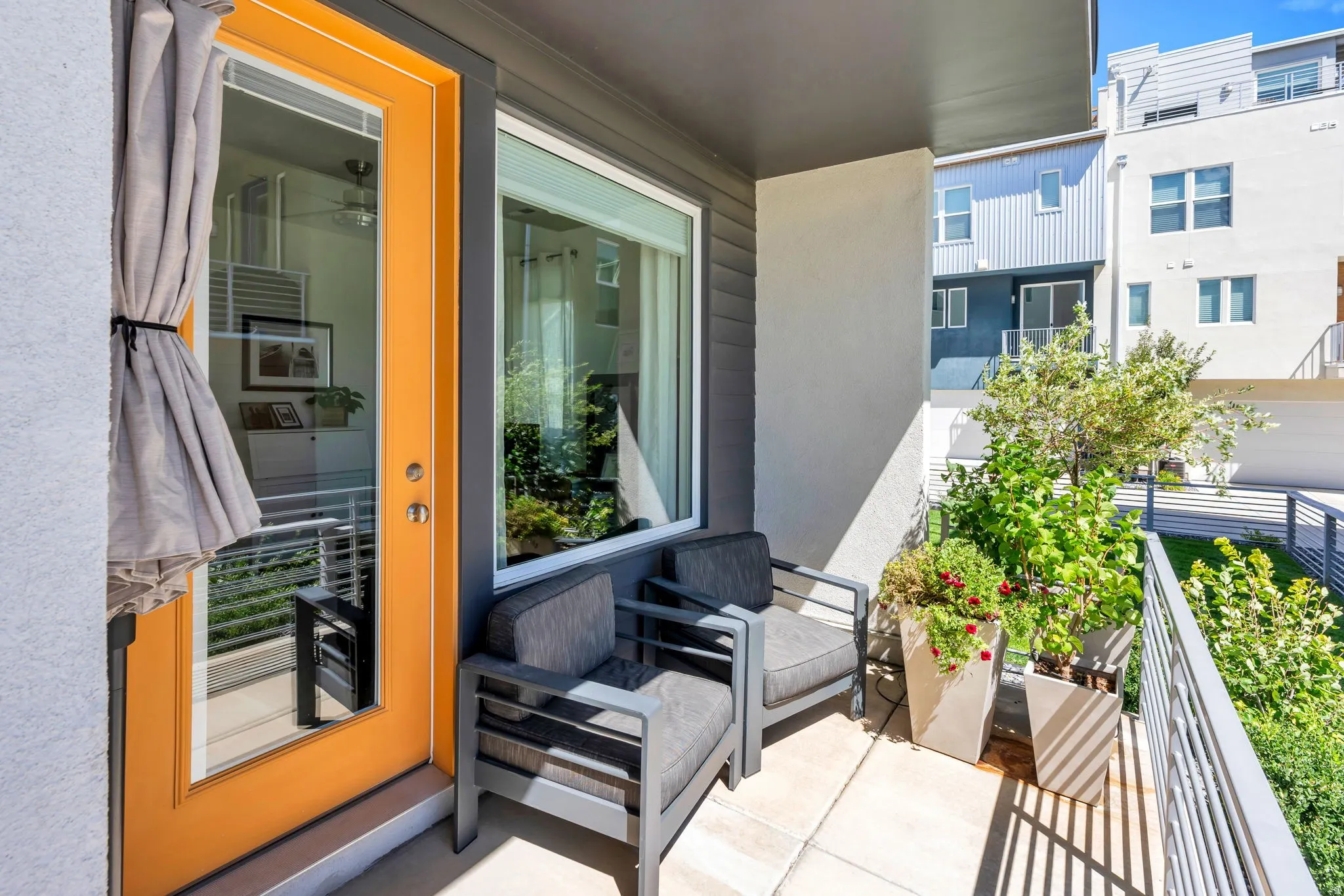 Private balcony with a vibrant orange door, concrete flooring, and metal railings