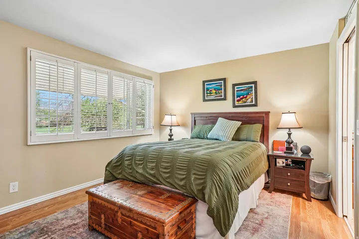 Wood-finish flooring, white window shutters, and a wood-panel headboard