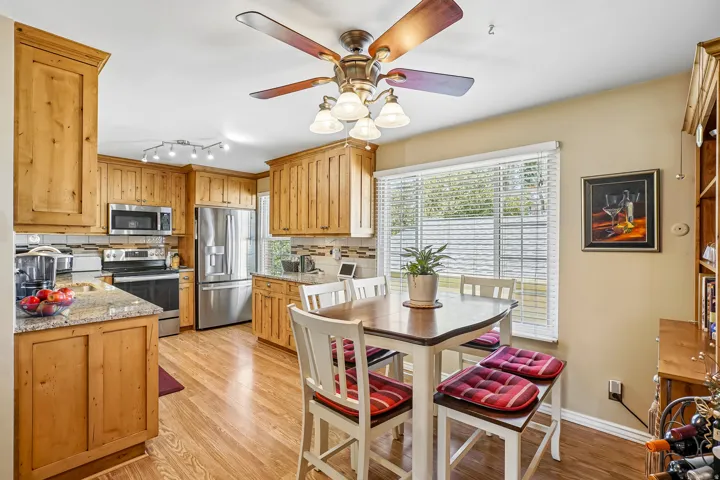 Kitchen featuring wood-finish cabinetry, granite-style countertops, stainless steel appliances, a tile backsplash, and wood-finish flooring