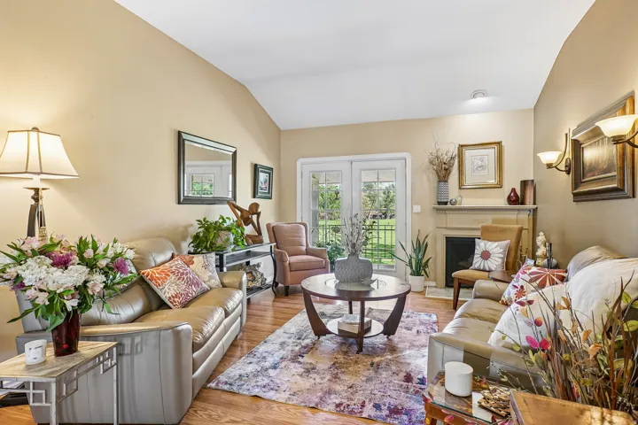 Vaulted ceiling living room featuring wood-finish flooring, a fireplace with a stone mantel, and double glass-paneled doors opening to the exterior