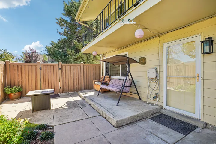 Concrete patio area with wood fence, wood-paneled exterior, and upper-level balcony with black iron railing
