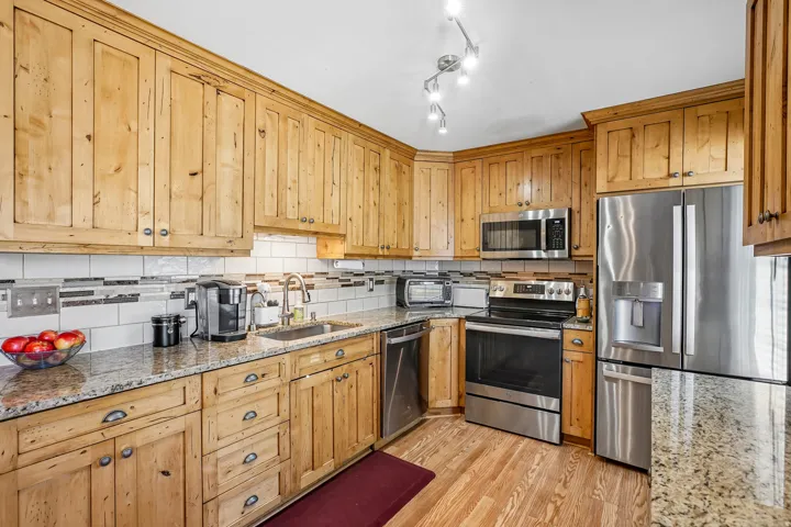 Wood cabinetry with granite countertops, stainless steel appliances, tile backsplash, and track lighting