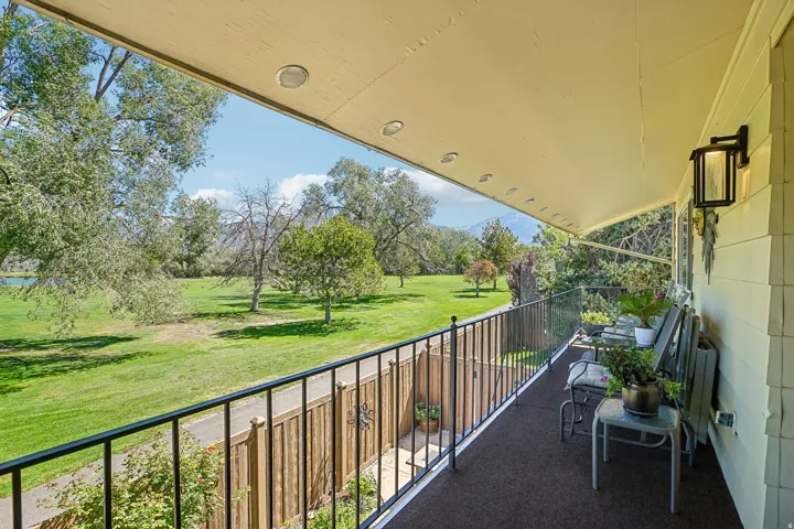 Covered balcony featuring recessed lighting, a black metal railing, and a wall-mounted light fixture overlooking a manicured lawn