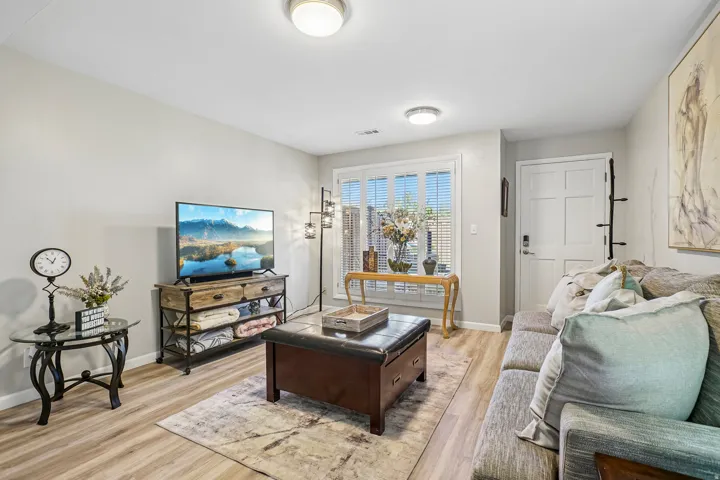 Living area with wood-finish flooring, white walls, and a multi-pane window with plantation shutters