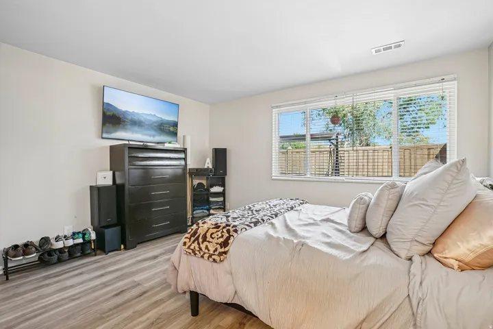 Wood-finish flooring throughout, bright white walls, and a large window with horizontal blinds