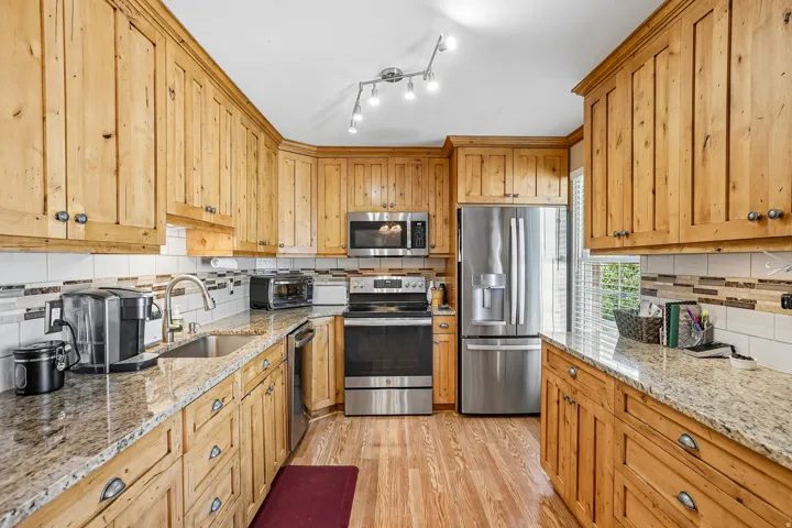 Wood-finish cabinetry with dark hardware, stone countertops, stainless steel appliances, and a mosaic tile backsplash