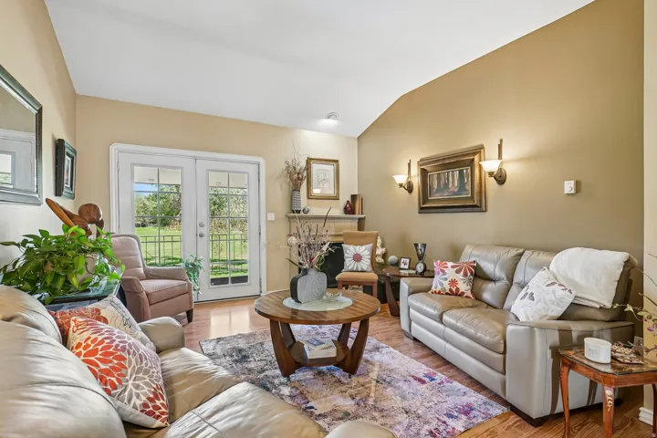 Vaulted ceiling, French doors with exterior access, sconce lighting, fireplace with stone mantel, and wood-finish flooring
