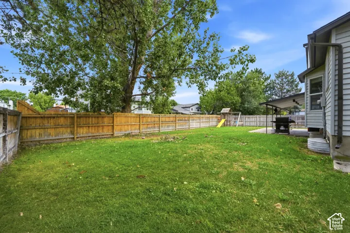 Expansive grassy yard with wood fencing, mature trees, and a covered patio area