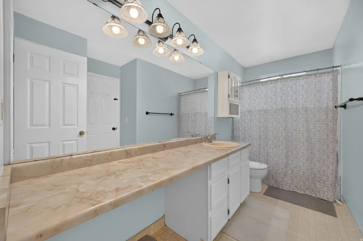Full-width vanity mirror, extended countertop, white cabinetry, integrated sink, and track lighting fixture