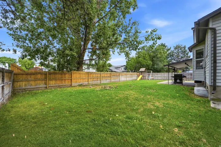 Expansive grassy yard with wood fencing, mature trees, and a covered patio area