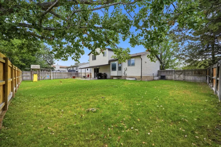Expansive fenced backyard with a grassy lawn, mature trees, and a covered patio area