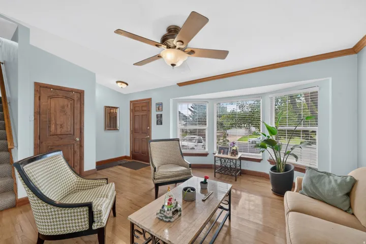 Hardwood-style flooring, a bay window with window treatments, a ceiling fan with integrated lighting, and crown molding