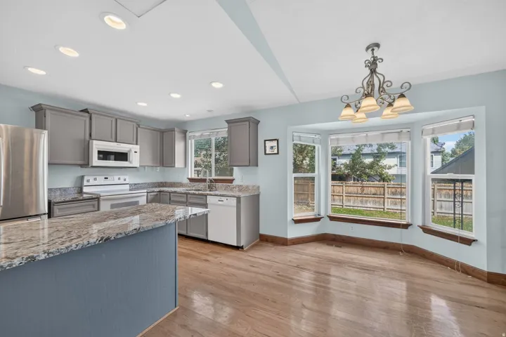 Kitchen featuring granite countertops, wood-finish flooring, recessed lighting, and a bay window with a decorative chandelier