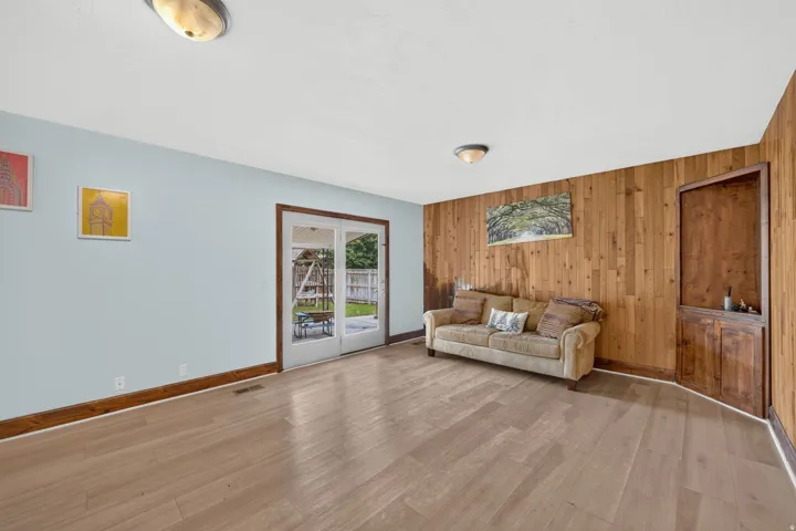 Light wood-finish flooring, light blue wall, wood paneling accent wall, built-in wooden cabinetry, and double glass-paneled doors