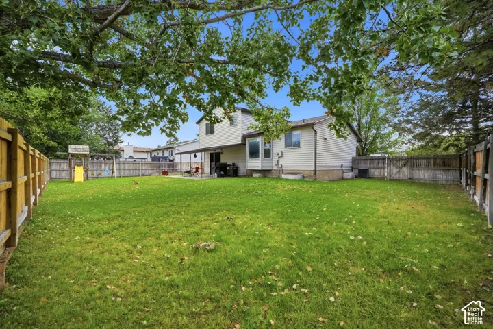 Expansive fenced backyard with a grassy lawn, mature trees, and a covered patio area