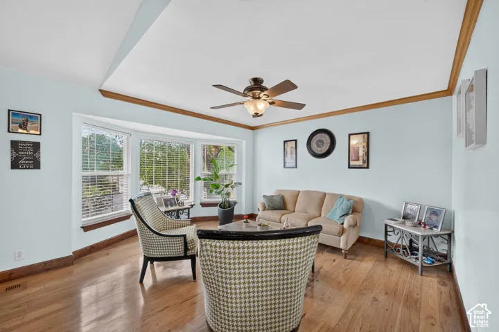 Bay window with blinds, wood-finish flooring, ceiling fan with integrated lighting, wood crown molding, and wood baseboards