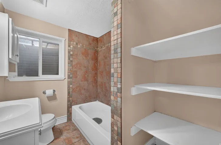 Built-in storage shelving, a tiled tub and shower combination, a single vanity with storage, and a window for natural light