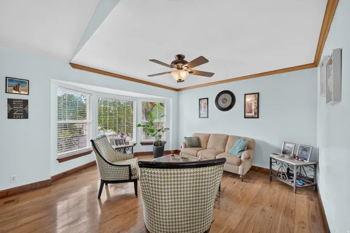 Bay window with blinds, wood-finish flooring, ceiling fan with integrated lighting, wood crown molding, and wood baseboards