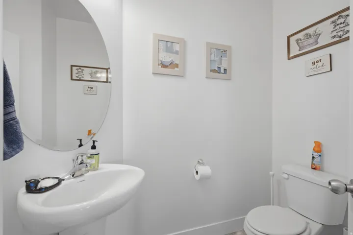White pedestal sink with a chrome faucet, oval wall mirror, and a white toilet