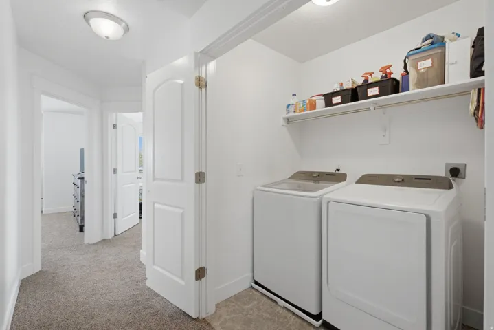 Dedicated laundry area with built-in shelving, overhead lighting, and carpeted hallway access