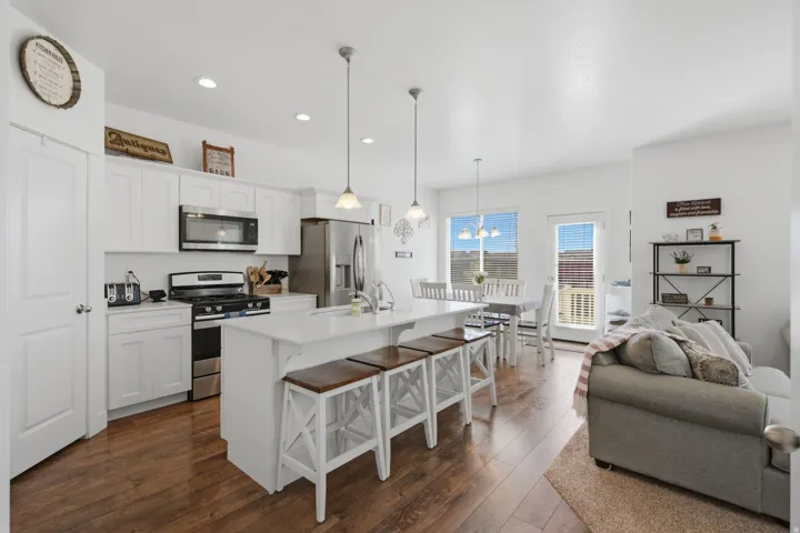 Open concept kitchen featuring white cabinetry, stainless steel appliances, a large island with seating, pendant lighting, and wood-finish flooring
