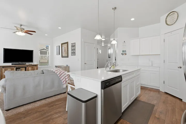Open-concept living space featuring wood-finish flooring, white cabinetry, a kitchen island with a stainless steel sink, recessed lighting, and a ceiling fan
