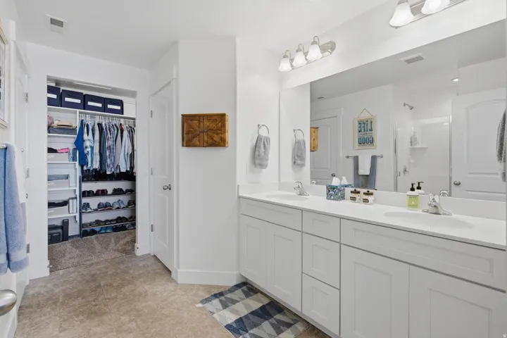 Dual vanity with white cabinetry and integrated sinks, large mirrored surface, vanity lighting, and an adjacent walk-in closet with built-in shelving