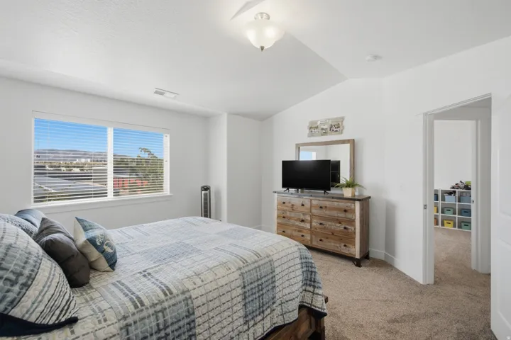 Spacious room featuring vaulted ceilings, a large window with blinds, and neutral carpeting